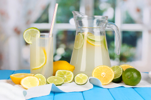 Citrus lemonade in pitcher and glass of citrus around on blue wo