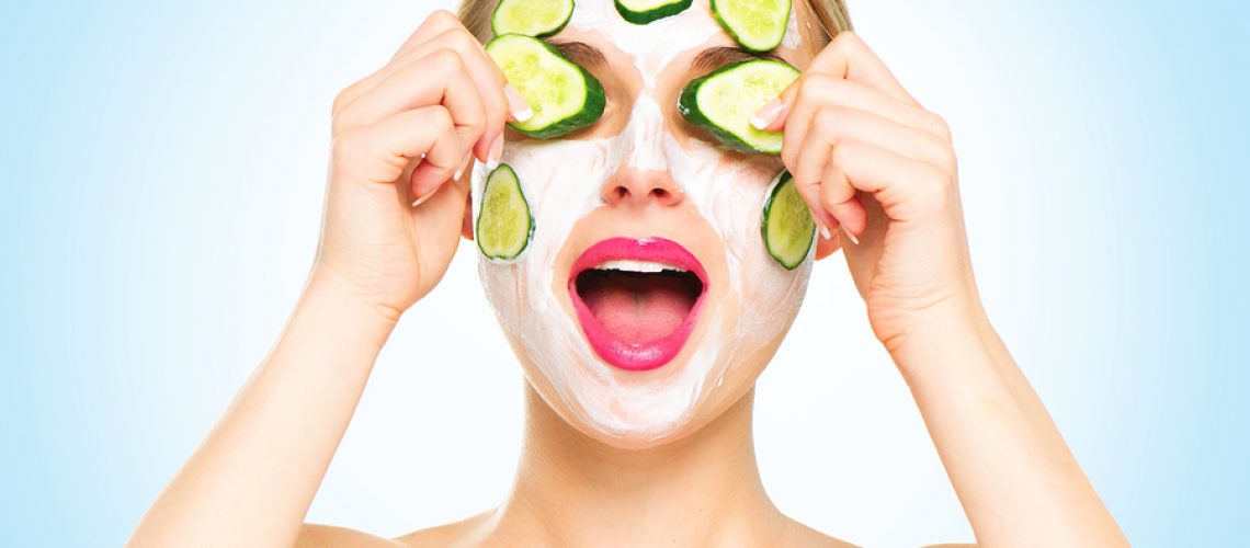 Funny smiling Spa Woman applying fresh Facial Mask with cucumbers. Beauty Treatments. Face mask, skin care concept. Beautiful Woman Applying Natural Homemade Facial Mask