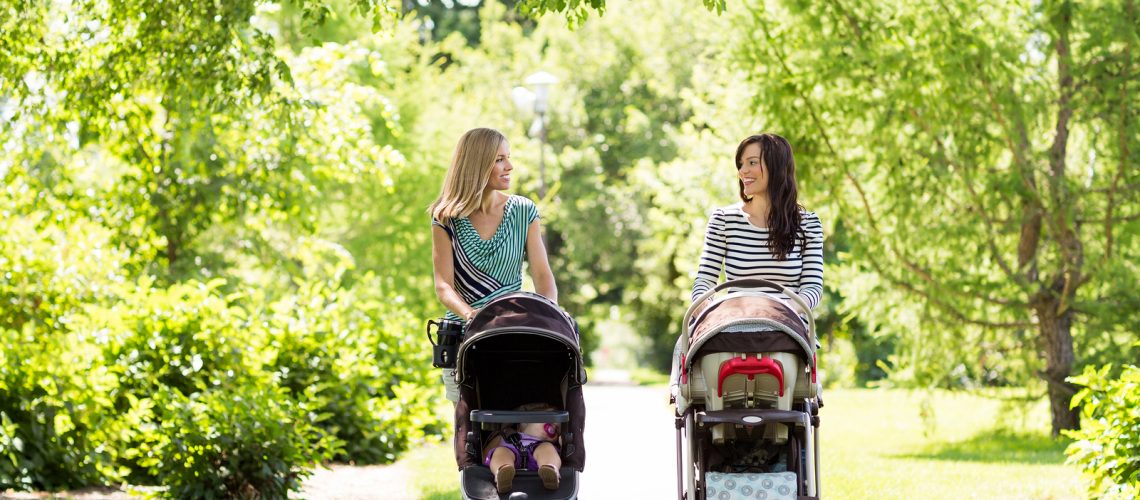 Happy mothers with their baby carriages walking together in park