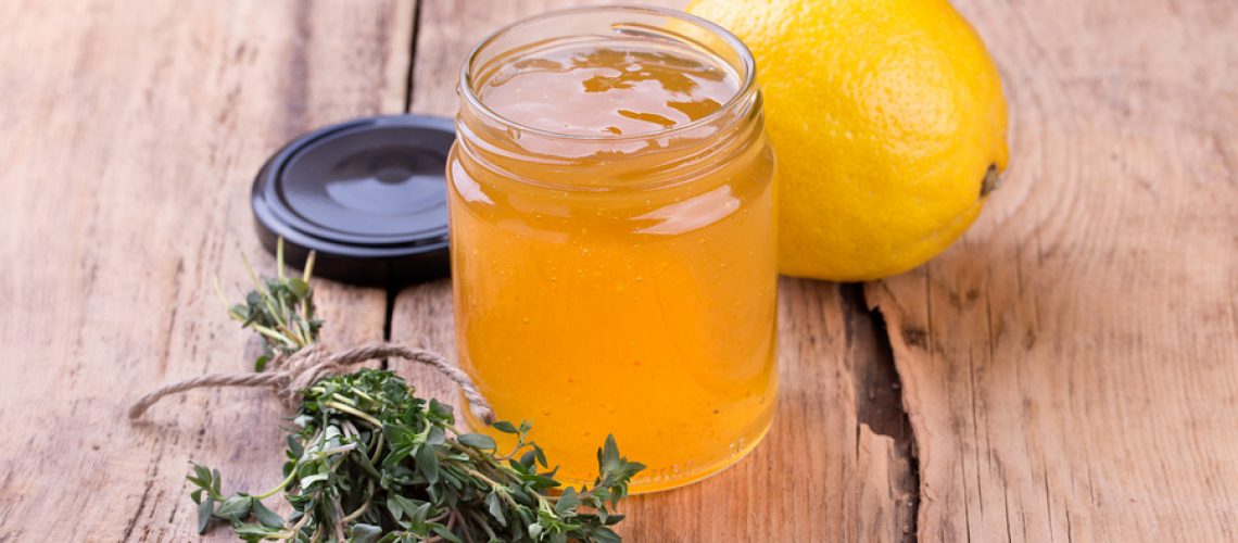 Colorful citrus jam in glass jar thyme and lemon on rustic wooden board