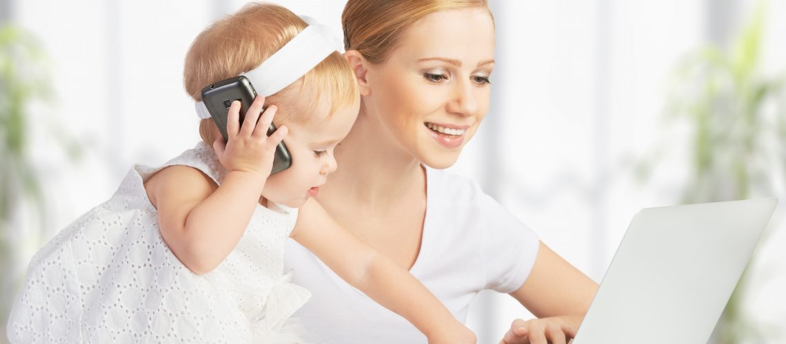 young mother with baby daughter works on the Internet with a computer and phone