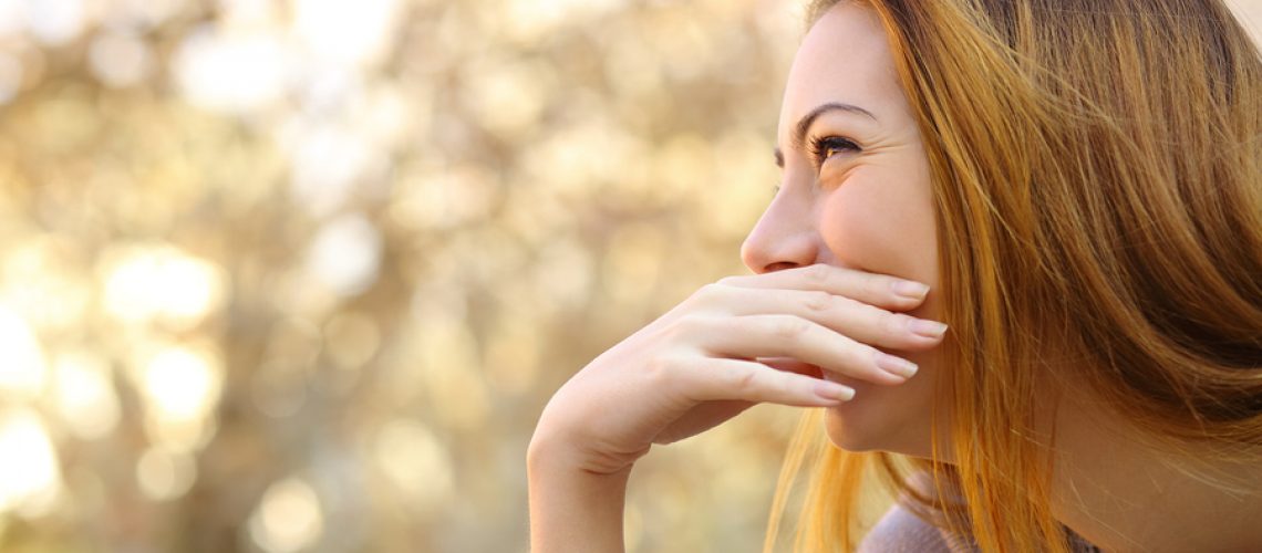 Happy woman laughing covering her mouth with a hand with a warmth background