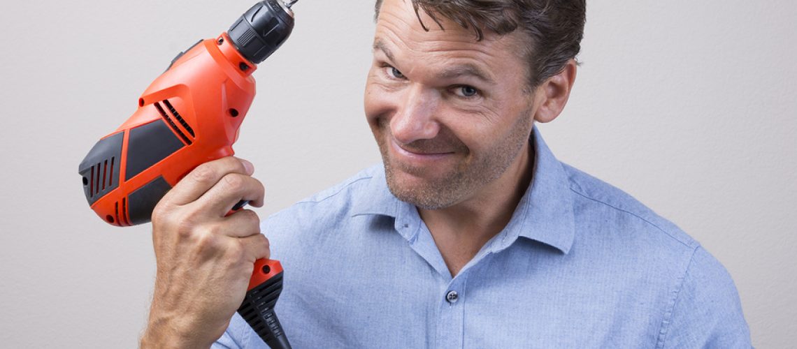 Closeup of handsome Caucasian man holding electric power drill with expression of readiness looking into camera