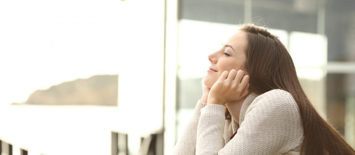 Side view portrait of a happy relaxed woman breathing fresh air outdoor in an hotel or apartment in the beach