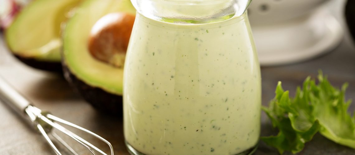 Homemade avocado ranch dressing in a small jar with fresh greens