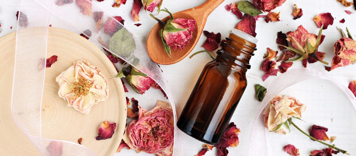 Essential rose oil, dried rose petals, aroma dropper bottle, wooden preparation utensils. Natural beauty care.